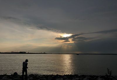 Silhouette people standing on beach against sky during sunset