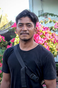 Portrait of young man standing against red flowering plants