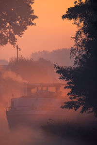 Silhouette of a cargo boat in the fiery red fog on a misty morning on the river during sunrise