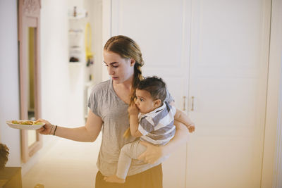 Mother carrying son while holding plate at home