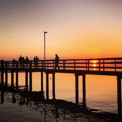 Silhouette people amidst sea on pier during sunset