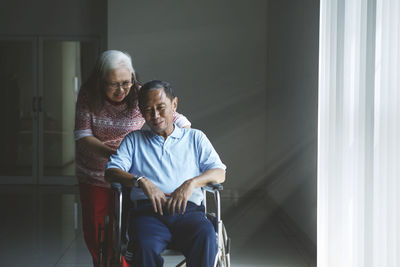 Smiling senior woman talking to man siting on wheelchair at home