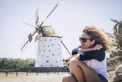 Side view of smiling young woman sitting against traditional windmill 