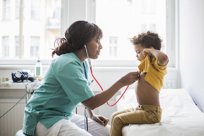 Female pediatrician examining boy's heartbeat in medical clinic