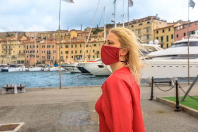 Low angle view of woman wearing mask looking away while standing against building