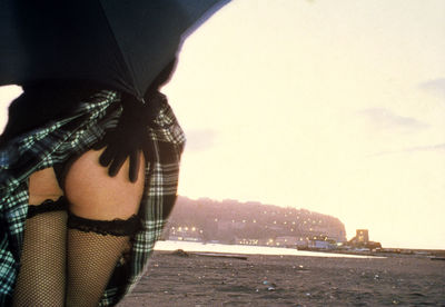 Midsection of seductive woman standing in front of lake against sky