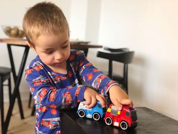 Cute boy playing with toy cars on table at home