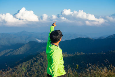 Side view of man with hand raised standing on mountain against cloudy sky