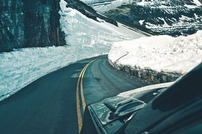 Road amidst snowcapped mountains seen through car windshield