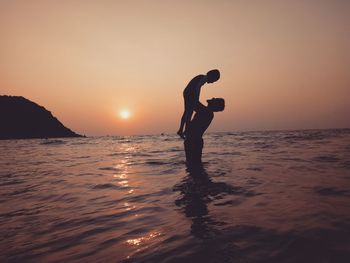 Silhouette people on sea against sky during sunset