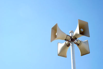 Low angle view of megaphones on pole against clear blue sky