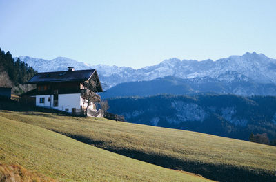 House on field by mountains against clear sky