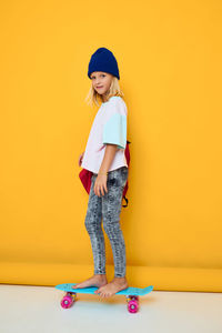 Portrait of young woman standing against yellow background