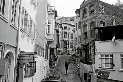 Rear view of woman with umbrella walking on street amidst buildings in city