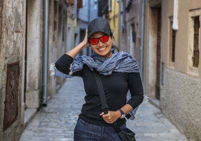 Woman wearing baseball cap and orange sunglasses in street alley