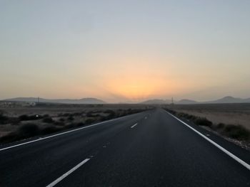 Empty road along landscape at sunset