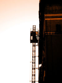 Low angle view of silhouette crane by building against clear sky