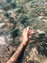 High angle view of inked female hand coming trough the sea water 