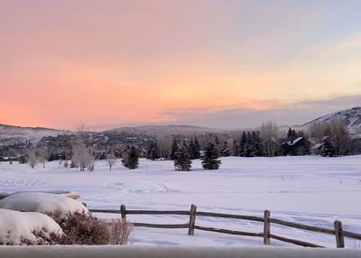 Snow covered field against sky during sunset