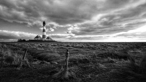 Lighthouse on field by building against sky