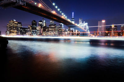 Illuminated city by sea against sky at night