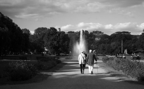 Rear view of senior couple walking on footpath in park against sky