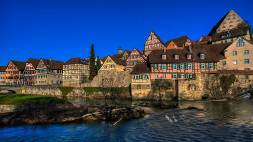 Buildings by river against clear blue sky