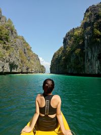 Rear view of young woman on rock by sea against clear sky