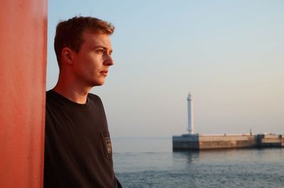 Portrait of young man looking away at sea against sky