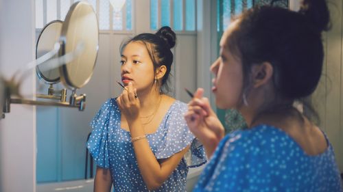 Woman applying make-up in front of mirror