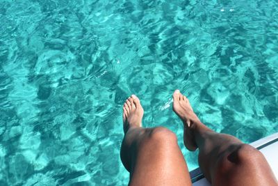 Low section of woman sitting on boat over turquoise sea