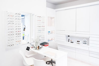 Rack with various glasses hanging over desk in light optician office in ophthalmology clinic