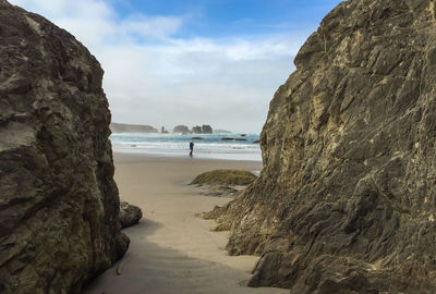 Mid distance view of senior man walking at beach against cloudy sky