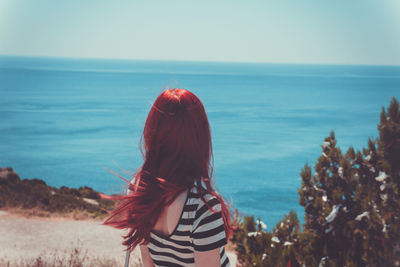 Rear view of woman standing by sea against sky