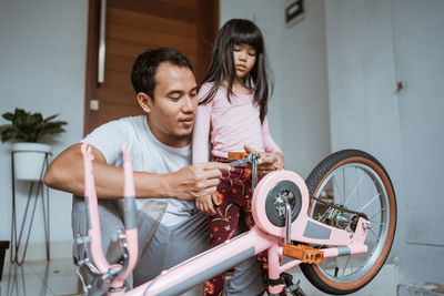 Father repairing bicycle with daughter at home