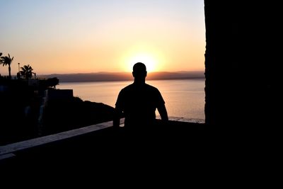 Silhouette man looking at sea against sky during sunset