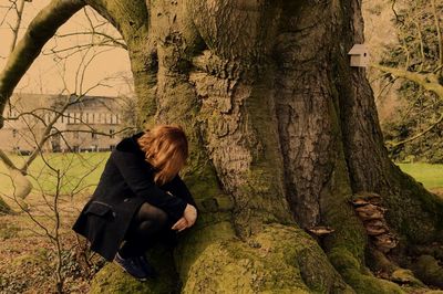 Depressed woman crouching on tree trunk at park