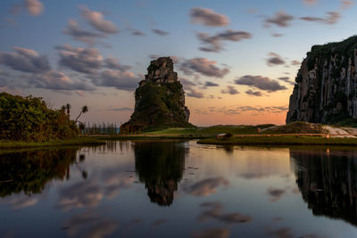 Scenic view of rock formations by lake against cloudy sky during sunset