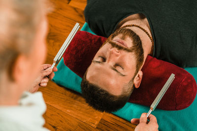 Therapist holding equipment by young man while performing music therapy at spa