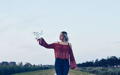 Digital composite image of butterflies flying by woman on field against sky