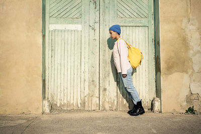 Woman with backpack standing tilt by door during sunny day