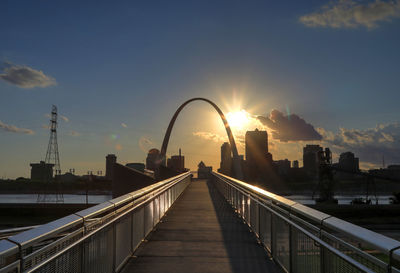 Footbridge over city against sky during sunset