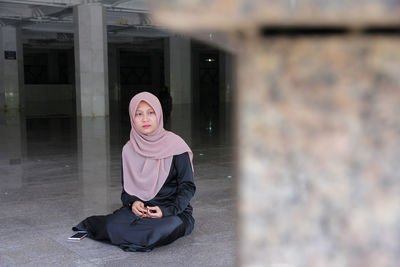 Full length of woman in hijab holding counting rosary beads while praying at mosque