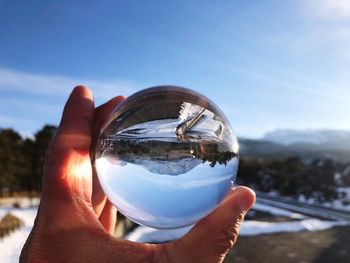 Midsection of person holding crystal ball against sky