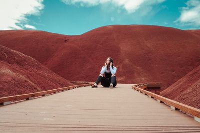 Woman sitting on footbridge amidst mountain against sky