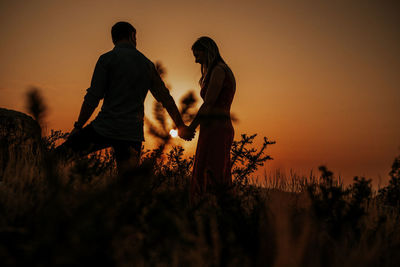 Side view of man standing on field against sky during sunset