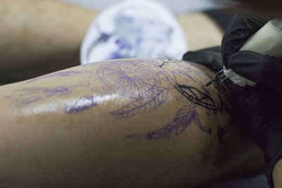 Cropped image of tattoo artist working on customer leg