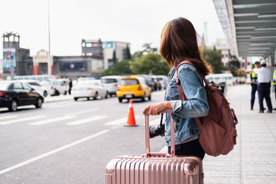 Side view of woman with luggage standing on street in city