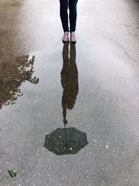 Low section of woman with umbrella reflecting on puddle during rainy season