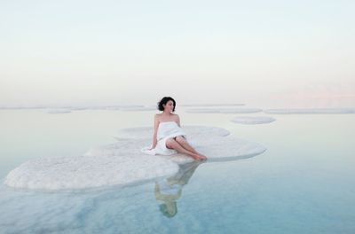 Full length of young woman sitting at sea